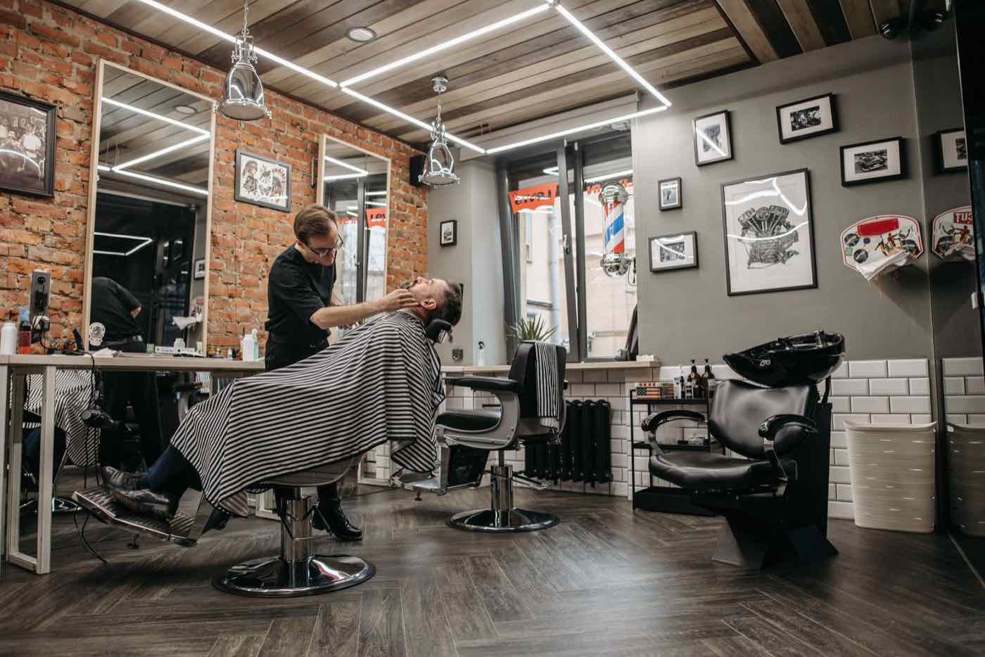 Barber rasiert einen Kunden im modernen Barbershop mit Backsteinwand